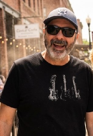 Labor day: the hands and hearts behind bhc Van devilder with sunglasses, black and white guitar tee shirt, and gray under armor hat while smiling at camera.
