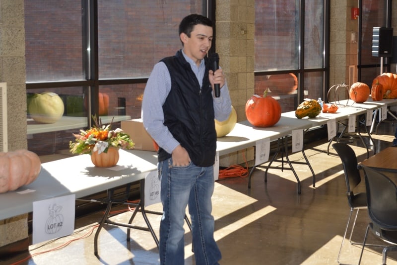 Male student with microphone talking in front of tables with pumpkins
