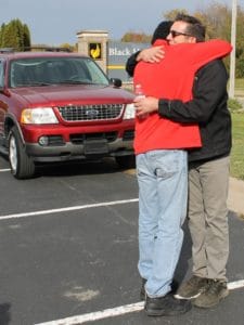 man in red jacket hugging man in black jacket in parking lot front of red Ford Explorer