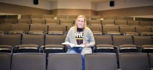 smiling college student sitting in auditorium with open textbook