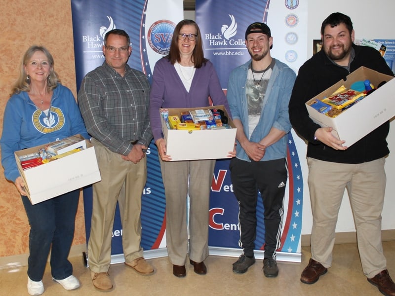 5 people looking at the camera with 3 holding boxes