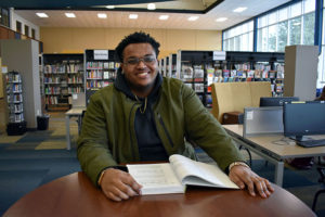 student sitting at table in library with book in front of him
