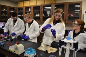 students in white lab coats conduct an experiment