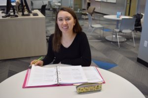 student sitting at table and smiling while turning a page in her binder