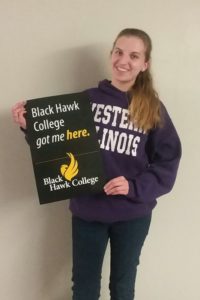 Lydia Olson wearing a purple Western Illinois University shirt and holding sign that says "Black Hawk College got me here"