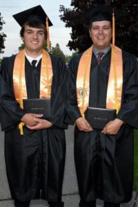 2 male grads wearing gold honors stoles and cords