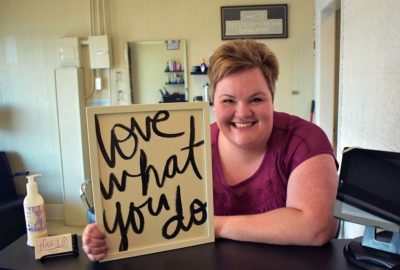 woman leaning on counter holding a sign that reads love what you do