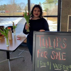 student holding a vase of tulips next to a Tulips for Sale sign