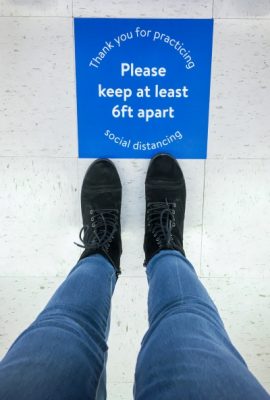 person's legs seen standing in front of social distancing sign on floor