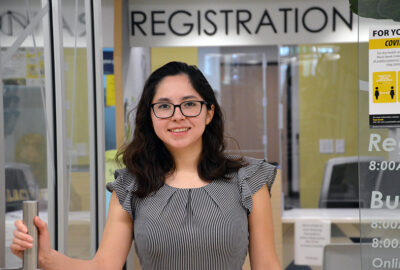 smiling female student holding a door handle with REGISTRATION sign above her