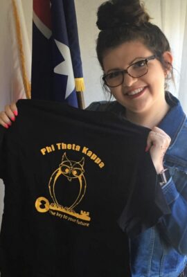 smiling student holding up a Phi Theta Kappa t-shirt