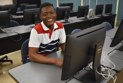 smiling male student sitting at a computer desk
