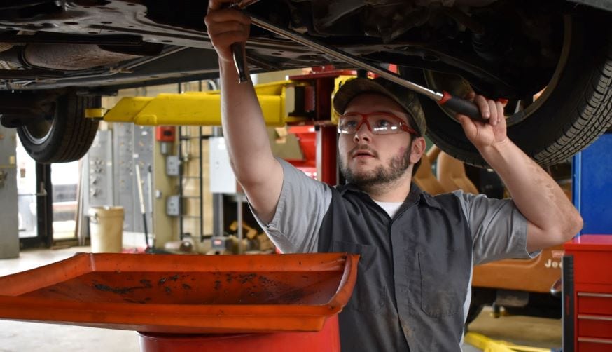 student in auto shop working on diesel engine while car is on a lift
