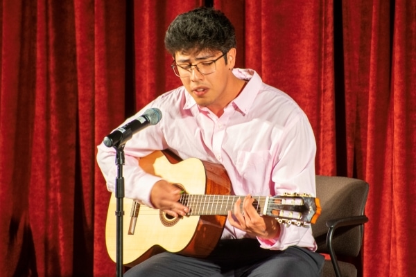 man seated playing guitar and singing