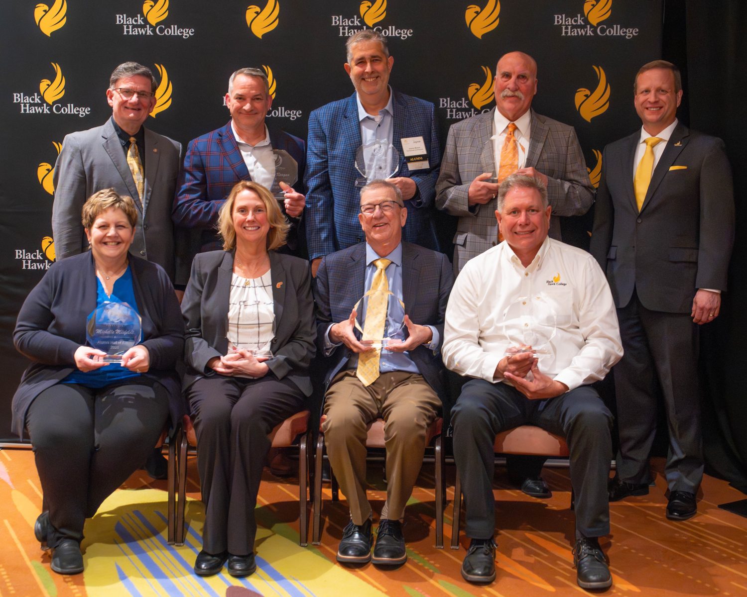 5 people standing and 4 people sitting with awards.