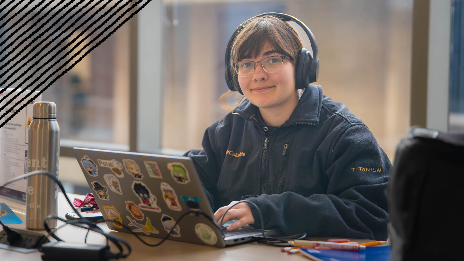 Female student sitting at a table with a laptop and wearing headphones.