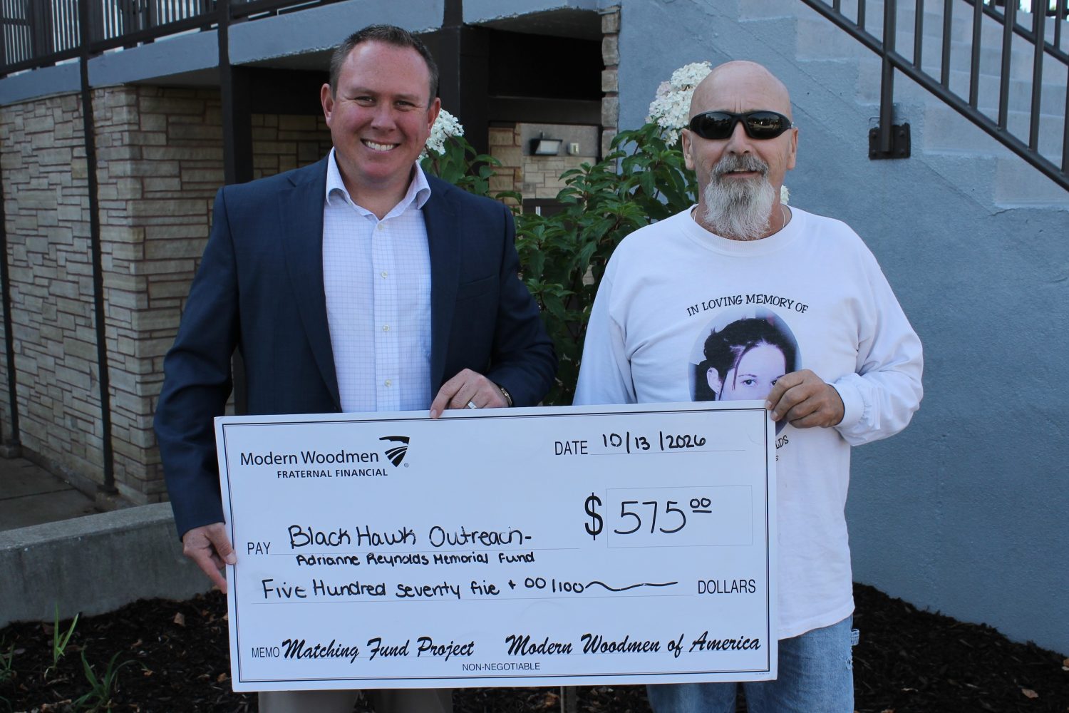 Reynolds family donates $1,718 to help ged® students 2 people holding an oversized check and standing by outdoor stairs going into bhc outreach center.