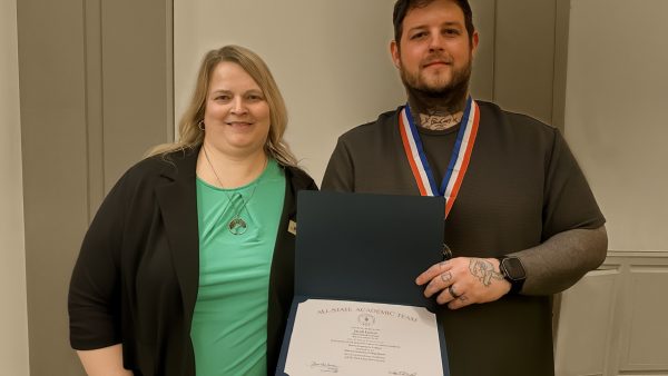 2 people standing in front of a wall, holding a certificate and smiling at the camera.