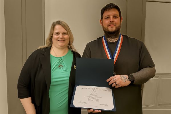 2 people standing in front of a wall, holding a certificate and smiling at the camera.
