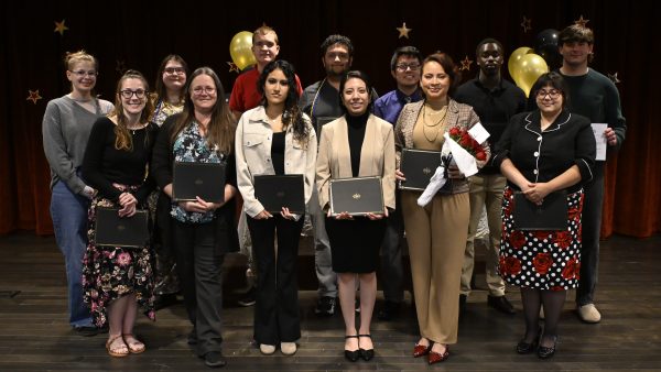 13 people standing on a stage holding certificates and smiling at camera.