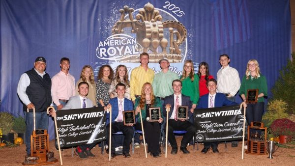 14 livestock judging team members and 2 coaches in front of large backdrop with awards.