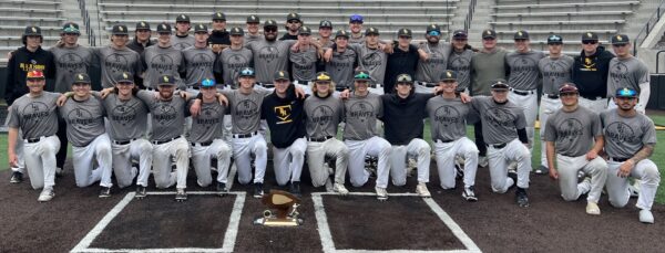 More than 30 baseball players in uniform posing on field with award.