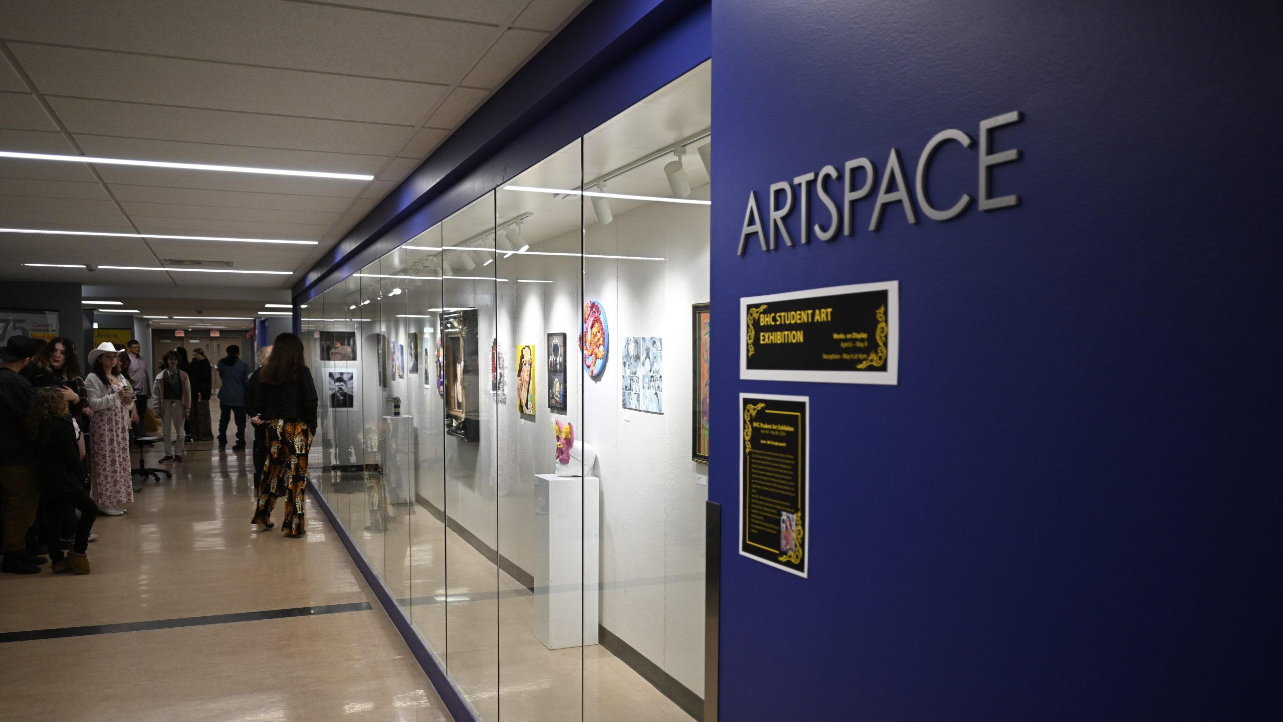 wall of art displayed behind glass with text ArtSpace on the wall.