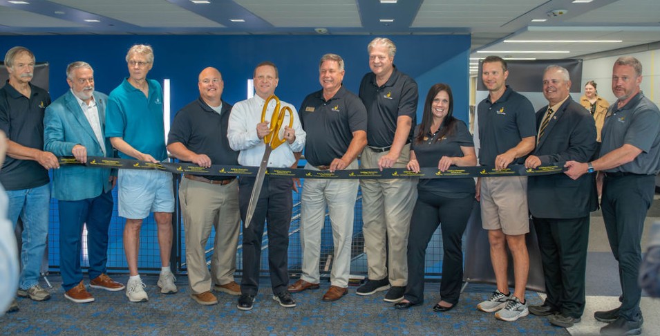 Bhc, community celebrate building 2 renovation 11 people in a line holding a ribbon with one man cutting ribbon with oversized scissors.