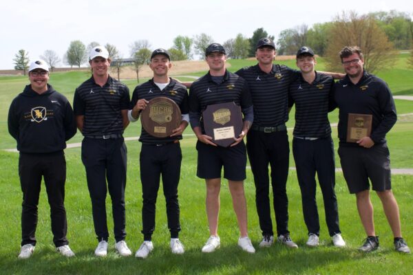 5 golf players and 2 coaches holding awards on green at golf course.