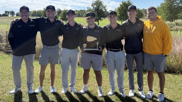 5 golfers and 2 coaches standing on golf course with trophy.