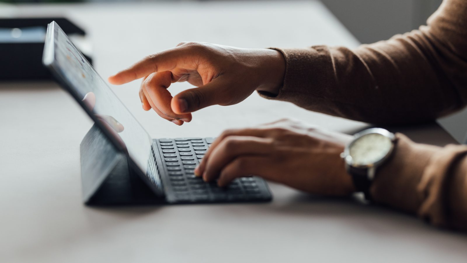 Close-up of hands operating a tablet with a keyboard in a professional office setting, highlighting digital interaction and technology use.