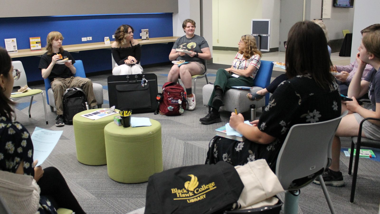 Group of people sitting in circle discussing books and eating pizza.