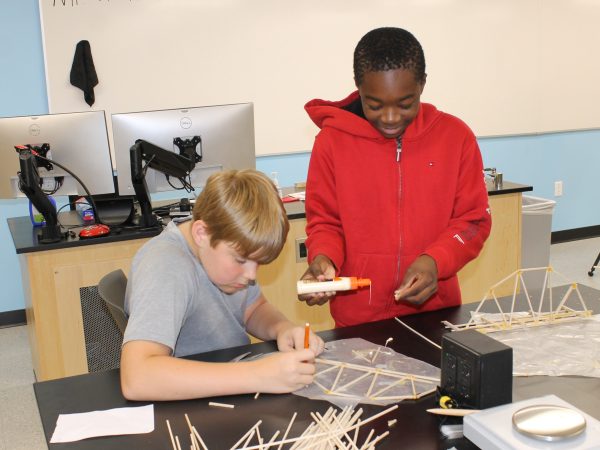 Two boys in physics world architecture forces gluing wooden sticks together.