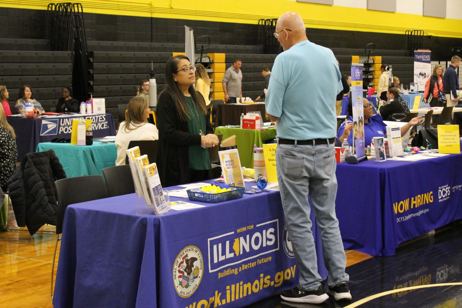 2026 career fair 2 people standing across from each other and talking at a table in a gym.