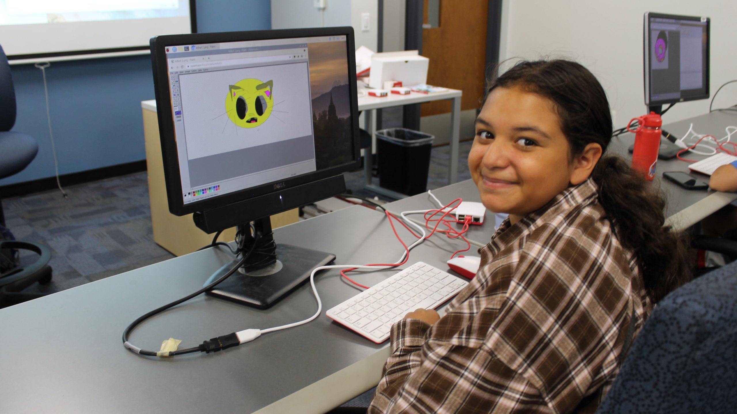 Girl sitting in front of computer and smiling at camera.