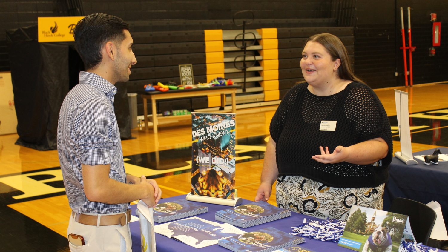 2 people standing and talking at a table at college night.