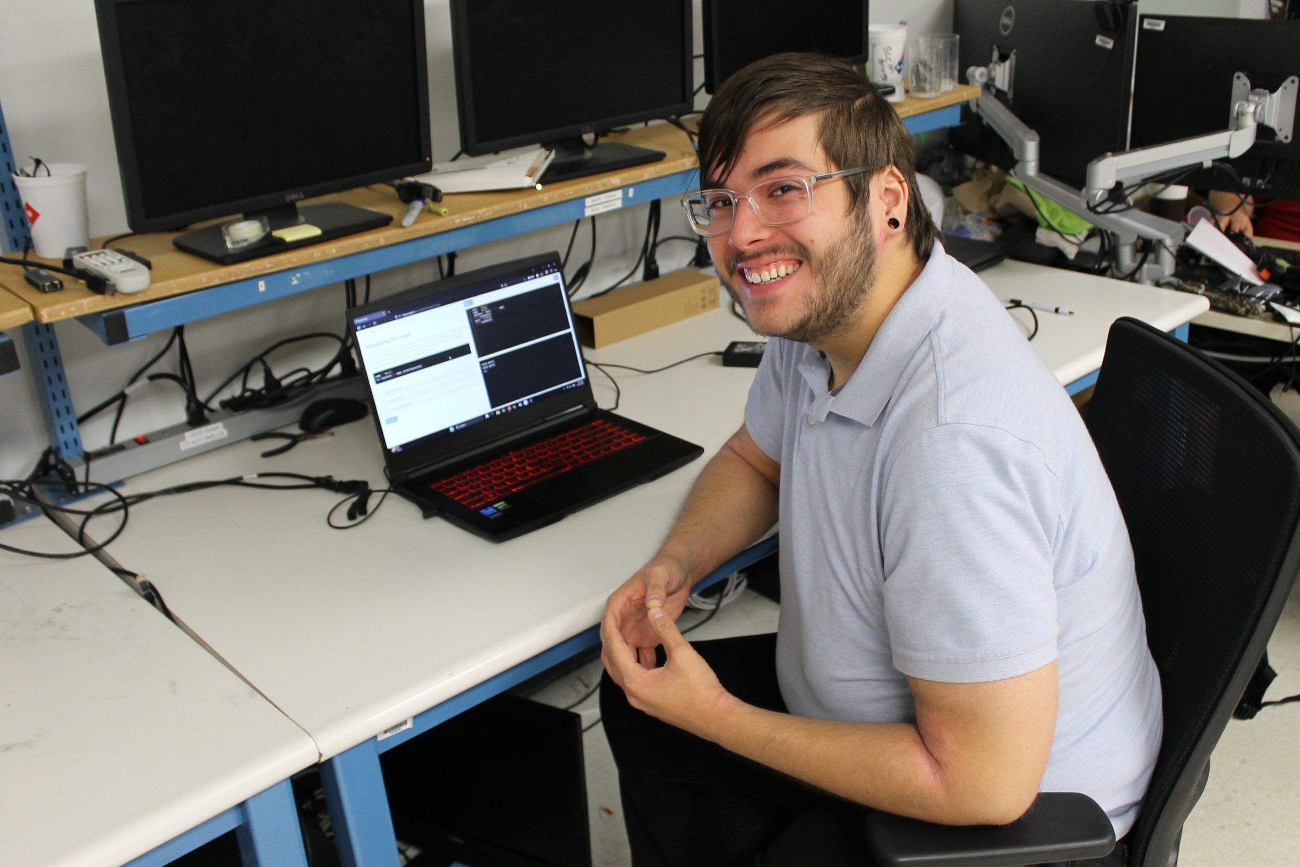 From high school dropout to honor student Man smiling at the camera while sitting at table with laptop and monitors.