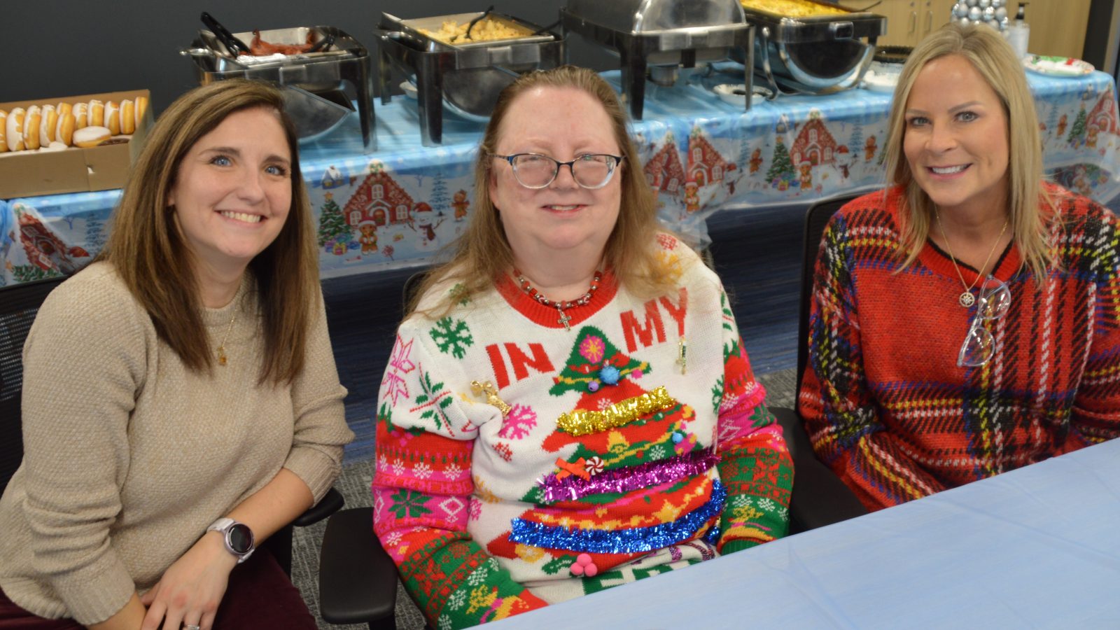 3 women seated at table and smiling at camera.