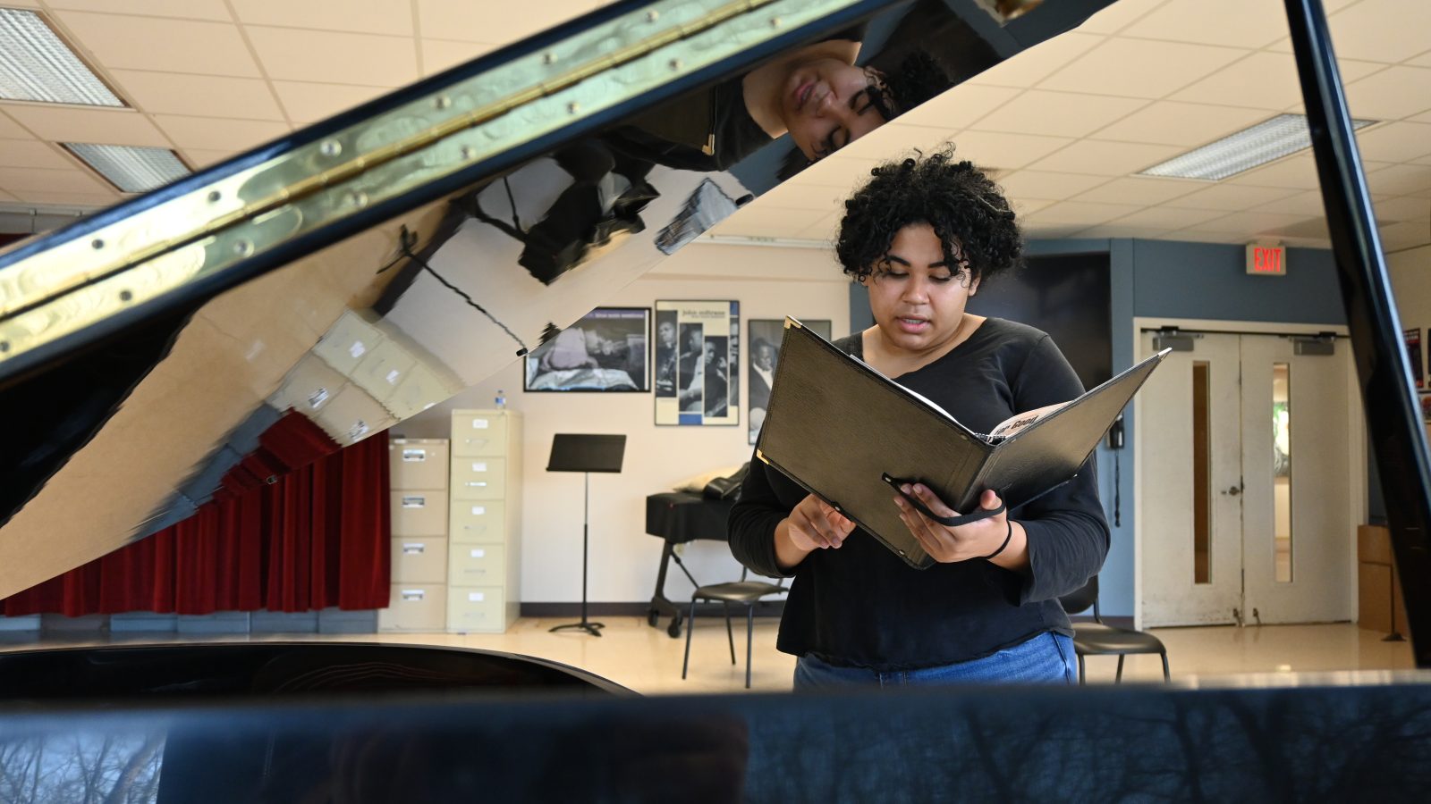 A girl behind a paino with her music folder ready to sing