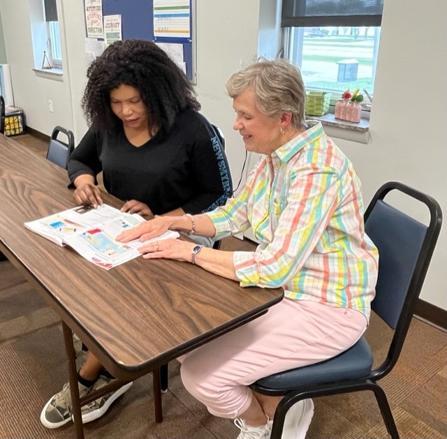 A person sitting at a table with a person looking at a piece of paper