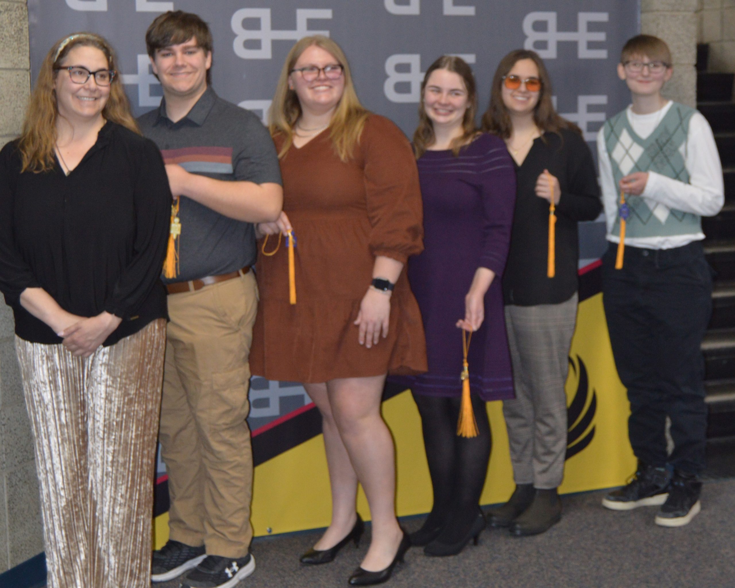 6 people standing in front of a backdrop and smiling at camera.