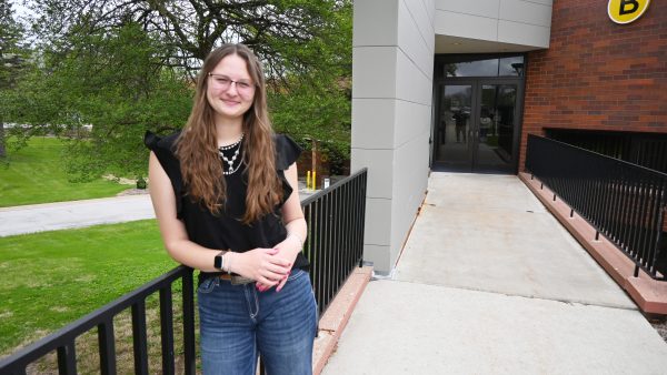 Female student leans on a railing outside a college building.
