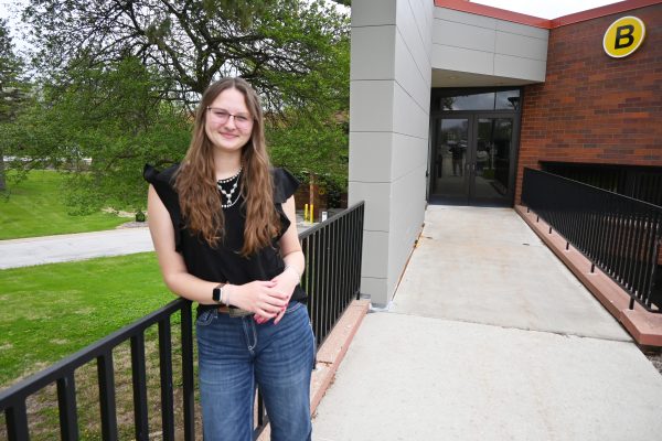 Female student leans on a railing outside a college building.
