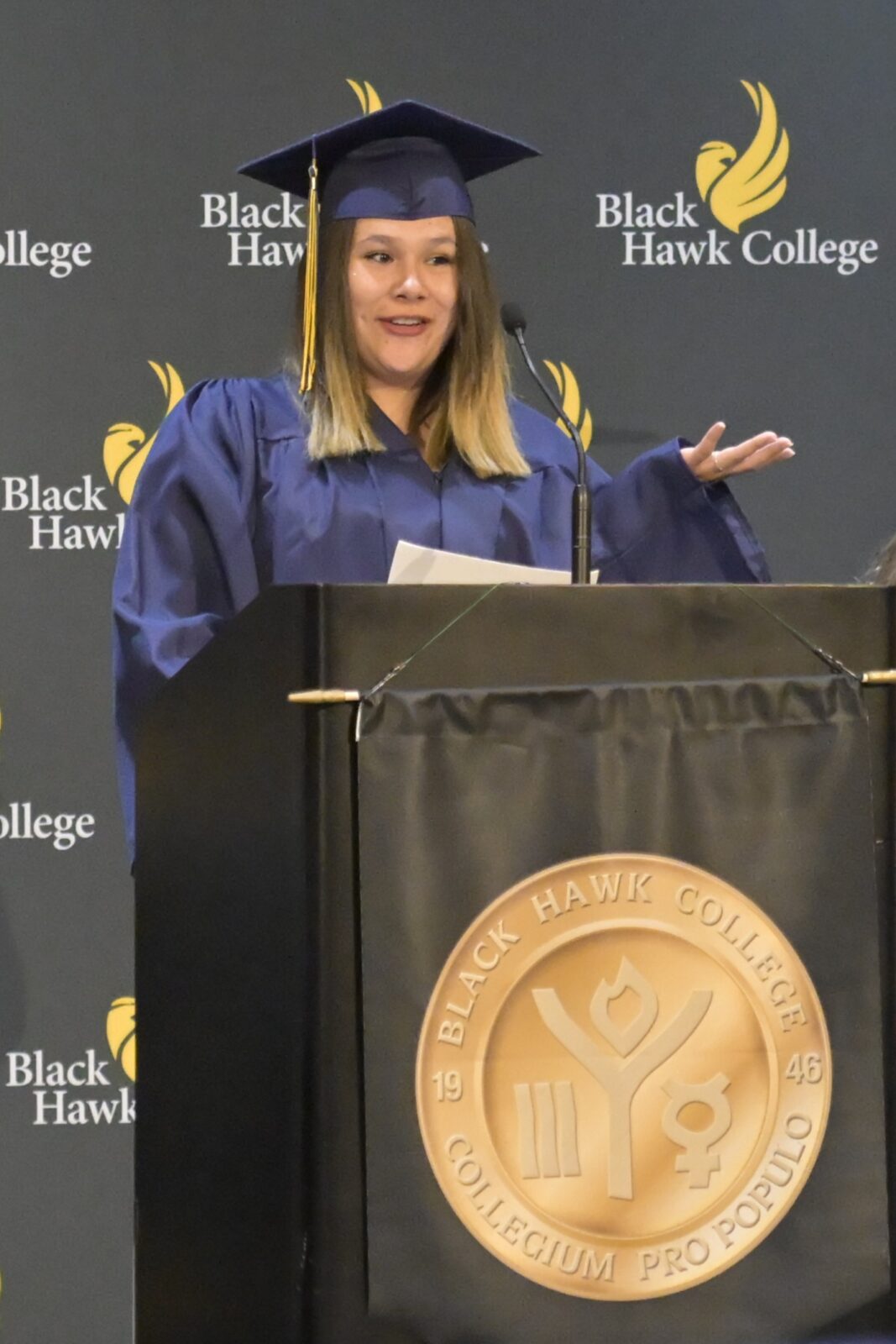 Woman in a graduation cap and gown standing at a podium.