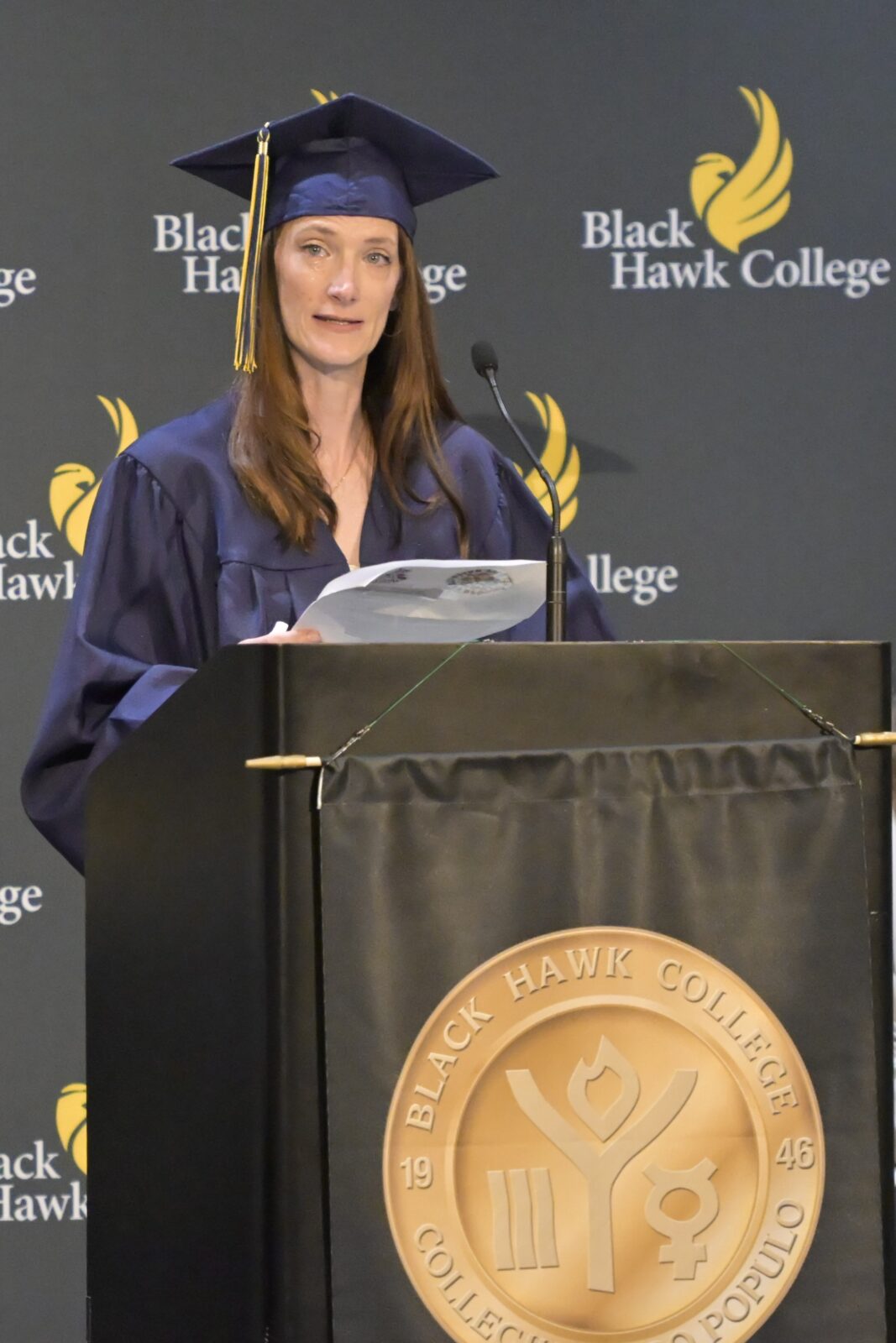 Woman in a graduation cap and gown standing at a podium.