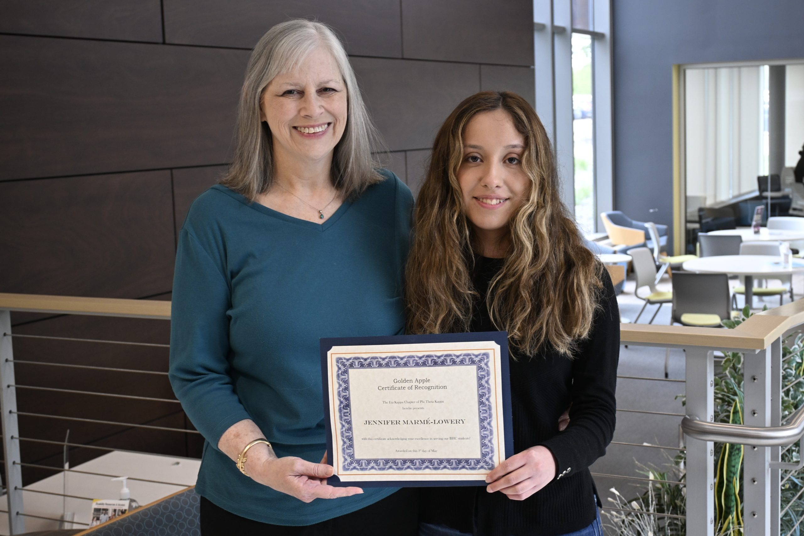 Two people standing, holding a certificate and smiling at the camera.