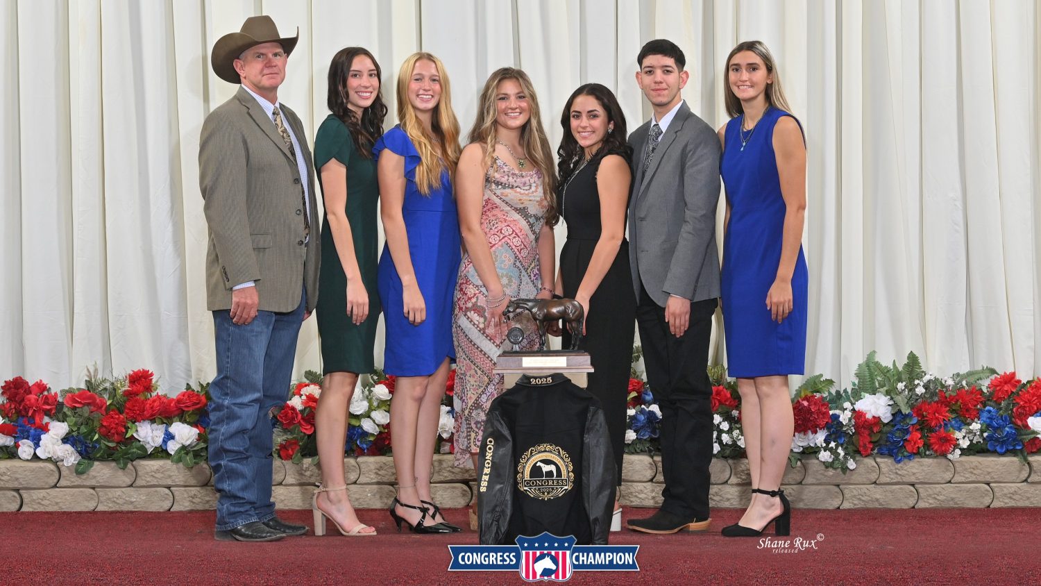 7 people standing with trophy and award jacket.