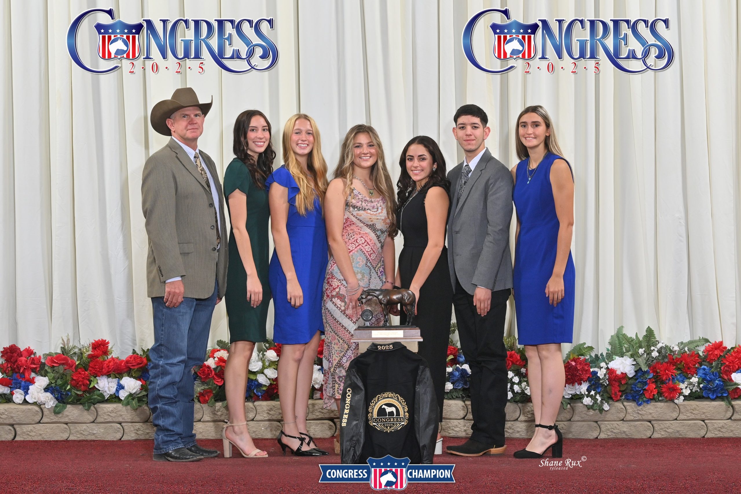 7 people standing with trophy and award jacket.