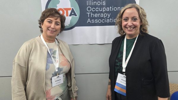 2 people smiling at camera while standing in front of wall with small banner.