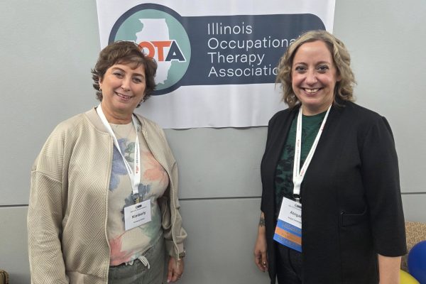 2 people smiling at camera while standing in front of wall with small banner.